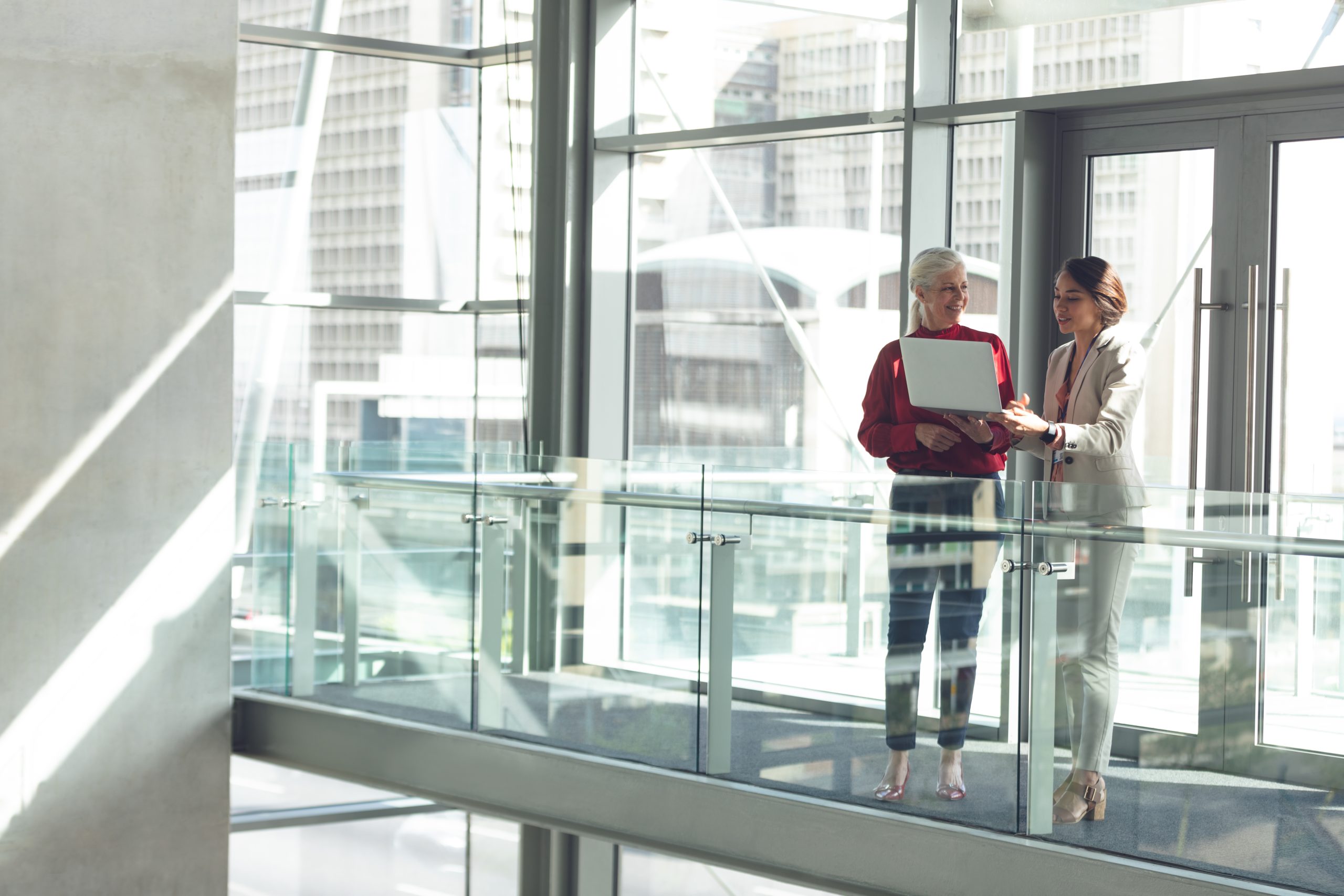 Two businesswomen reviewing a laptop in a modern office building.
