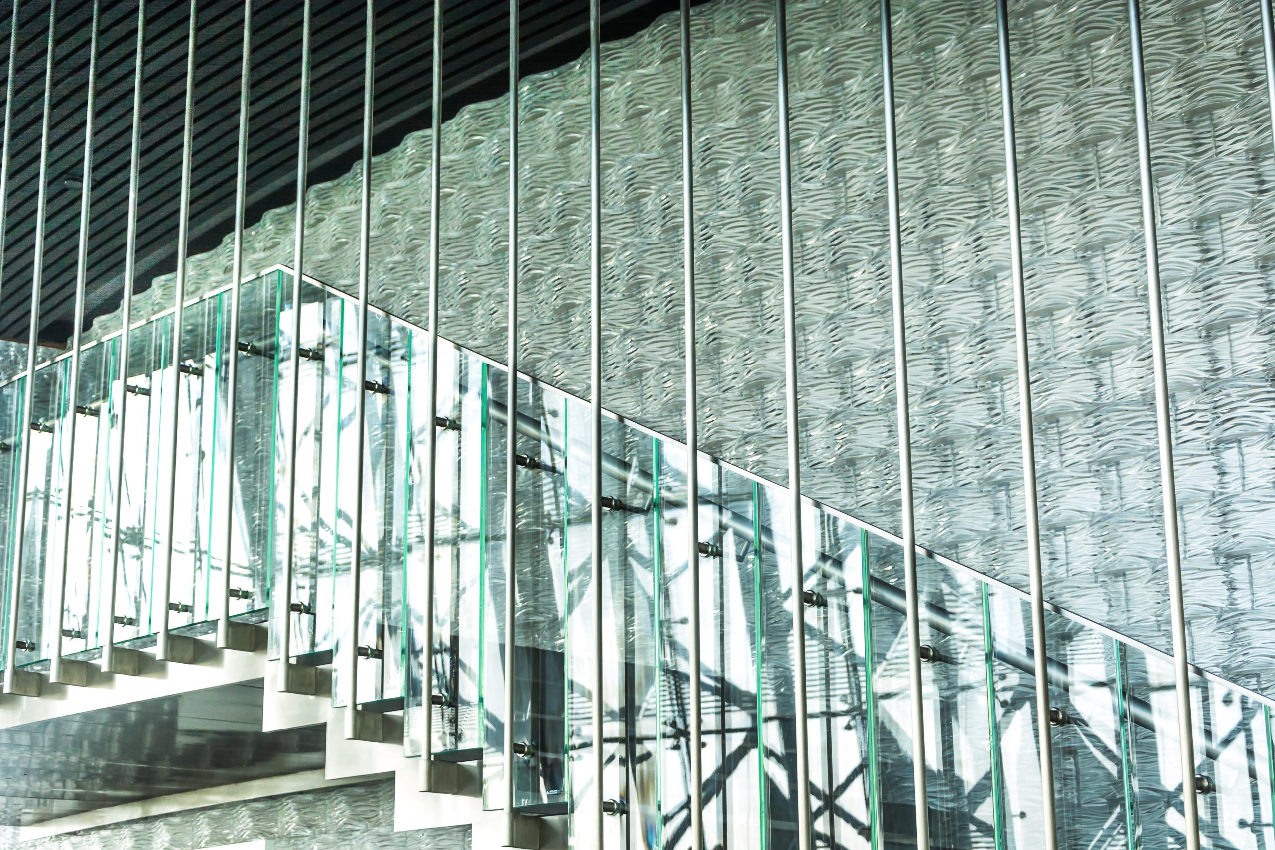 Modern staircase with glass railings and steel supports, reflecting light and creating a stylish architectural design.